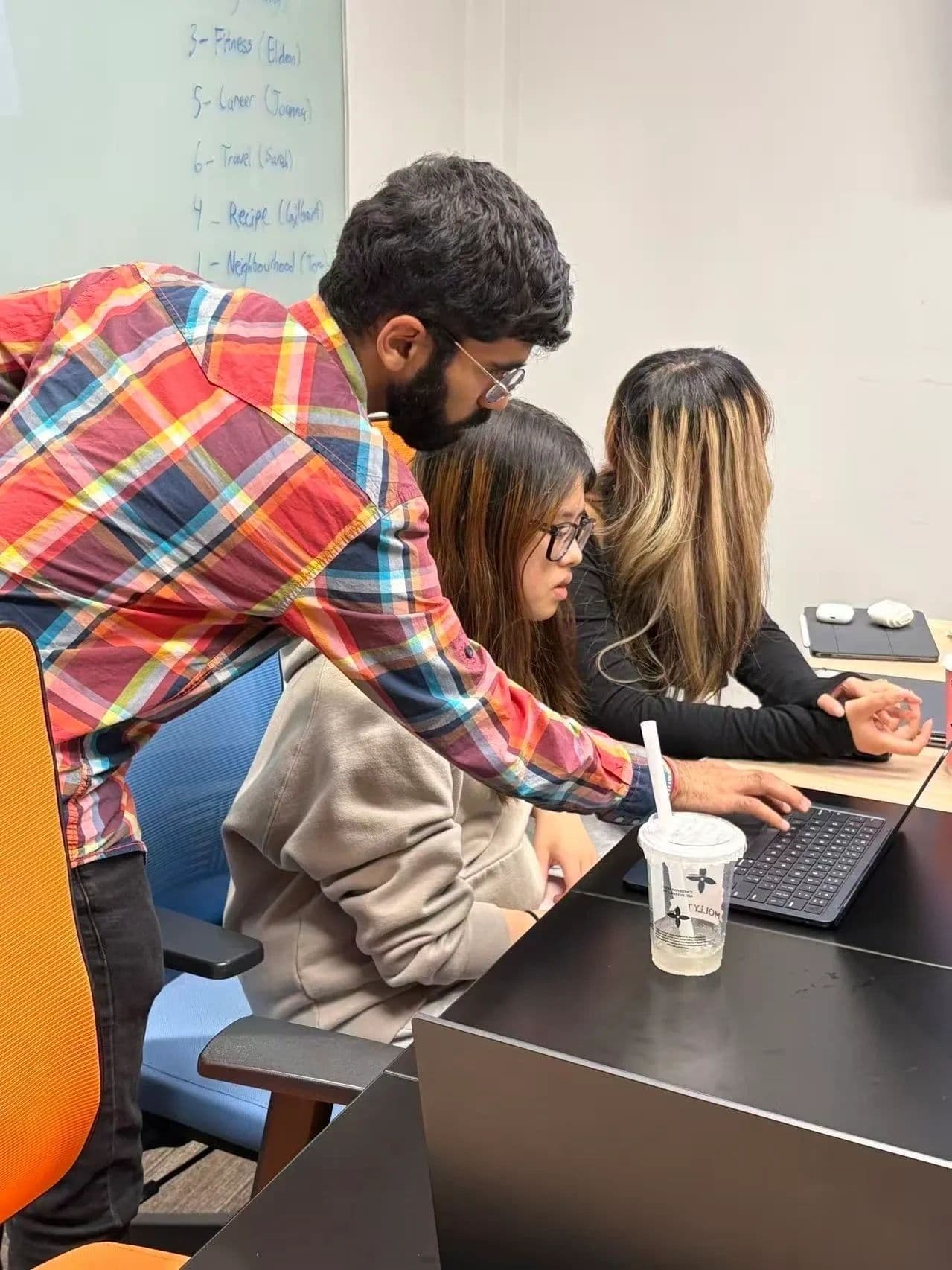 Mentor guiding students through research on laptops